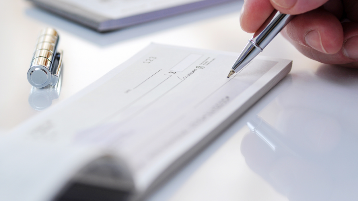 A close-up shot of a person writing a check with an expensive looking pen