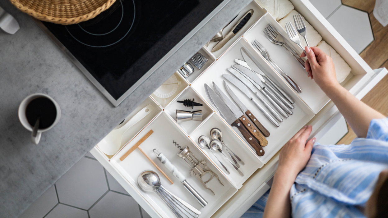 A top-down view of someone cleaning and organizing their silverware drawer.