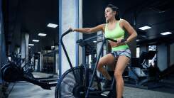 A woman in Spandex exercide gear works on an elliptical machine in an otherwise empty gym filled with workout equipment.