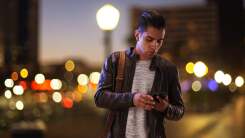 A man uses a smartphone while standing on a city street corner at night