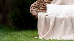 Wicker seat with blanket at pillows outside on grass