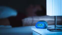 close-up of a digital clock at night, person sleeping in background