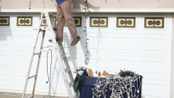 Person putting Christmas lights on house 