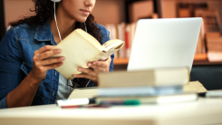 A person wearing headphones studying books and a computer, seated at a desk