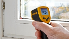 hand with infrared thermometer measuring temperature of window with mildew