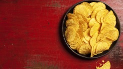 A bowl of yellow tortilla chips on a red table.