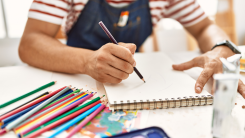 young man drawing in a sketchpad with colored pencils