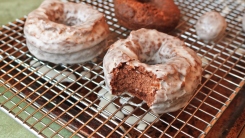 A bitten chocolate doughnut on a wire rack.