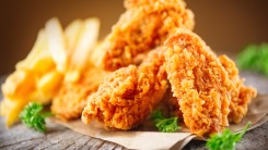 Fried chicken wings on a table with fries behind them.