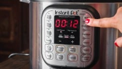 Close-up of a hand pressing a button on the panel of an Instant Pot