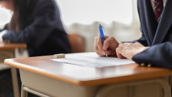 A photograph of a student at a wooden desk taking an exam