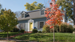 A photograph of a quaint blue house with a yellow door and a bright green lawn.