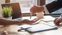 person  handing over keys to another person over desk 