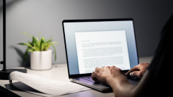 An over-the-shoulder photograph of a college student writing an essay on a laptop