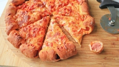 A pizza on a cutting board with a hot dog bit next to it.