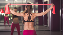 A woman in a workout studio doing a band pullapart exercise in front of a mirror