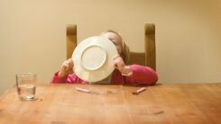 A little girl at the dinner table licking her plate