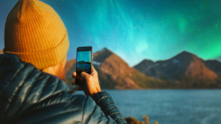 Man with smartphone taking photo of northern lights