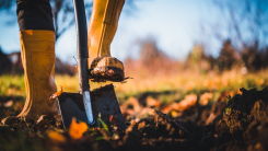 person wearing large rubber boots starting to dig with a shovel in a yard