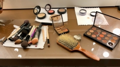 A table with assorted makeup and cosmetics, including brushes, palettes, etc.