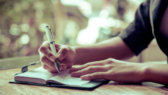 woman sitting at wooden table outside, writing in a journal