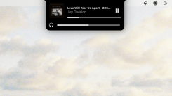 A black overlay extending from the menu bar showing the currently playing track (Love Will Tear Us Apart by Joy Division) and the current volume.