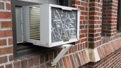 An old, scraped up AC window unit protruding from the window of an apartment building 