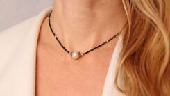 A closeup of a woman wearing a short necklace with a single pearl in the middle