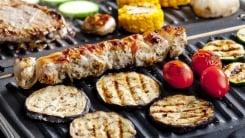 A close-up of meats and veggies on an indoor electric grill.