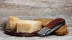 A pocket knife leaning on some bread next to hard cheese.