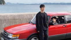 A still from Drive My Car of a character standing against a red car.