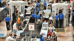 A photograph of passengers moving through the security line at a busy airport