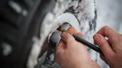 man's hands checking tire pressure in winter snow