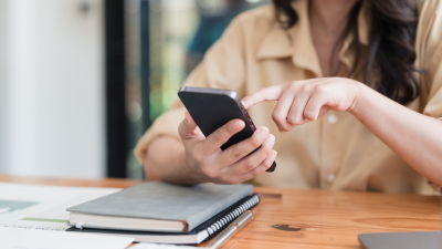 Woman looking at a phone and working in a small notebook