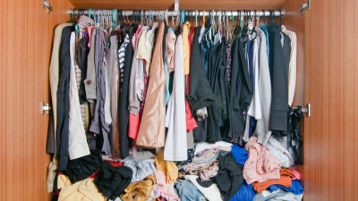 A photograph of a cramped, messy closet with a lot of clothes jammed in next to each other