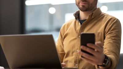 A man checking his phone and sitting in front of a laptop