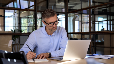 Business man looking at laptop, taking notes