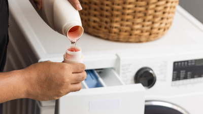 Someone pouring laundry detergent into a bottle cap in a laundry room