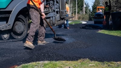 Construction worker shoveling freshly laid asphalt 