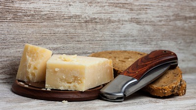 A pocket knife leaning on some bread next to hard cheese.