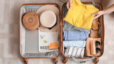 person packing summer clothing and accessories into a suitcase