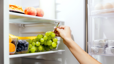 Hand reaching into a refrigerator to grab a bunch of grapes