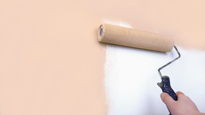 A hand using a paint roller to cover primer with peach colored paint