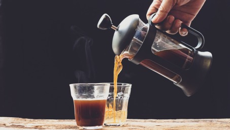 A hand pouring French press coffee into two glass cups.