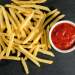 A pile of french fries next to a small bowl of ketchup