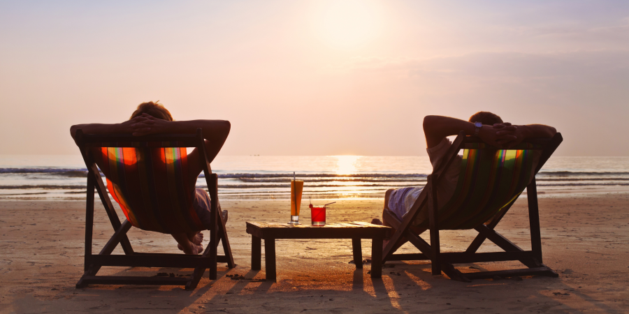 A couple relaxing in chairs on the beach with two cocktails on a table between them