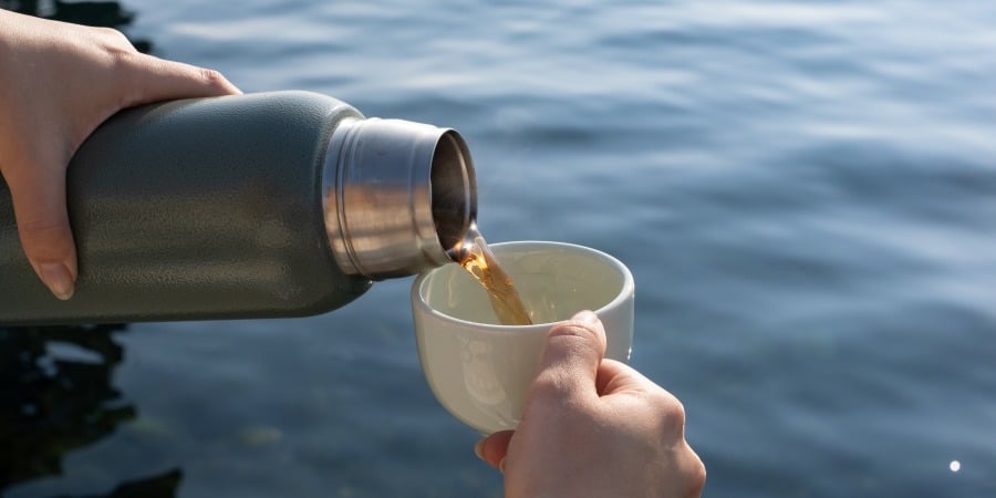 Person's hand pouring wine out of a thermos and into a mug.